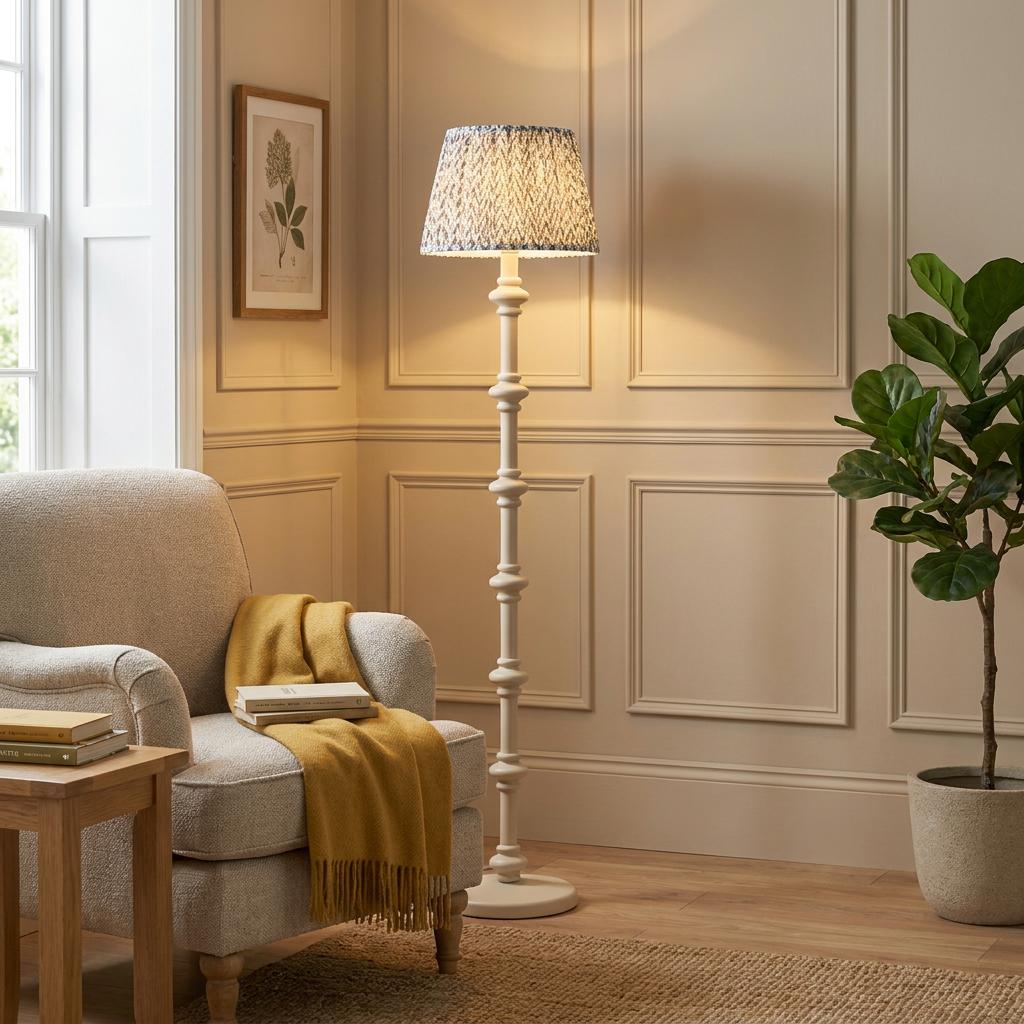 White turned wood floor lamp with a grey leaf pattern shade in a cozy living room next to an armchair.