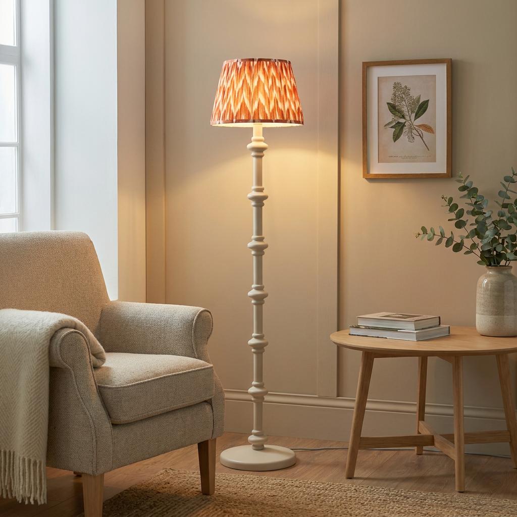 White spindle floor lamp with an apricot orange zigzag shade in a cozy living room corner with an armchair.