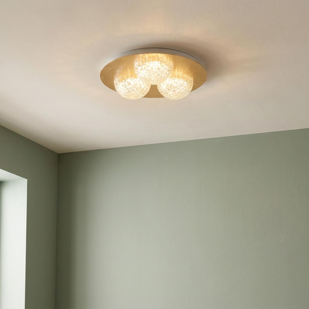 Gold flush ceiling light with three glowing textured acrylic globes, mounted in a room with light green walls.