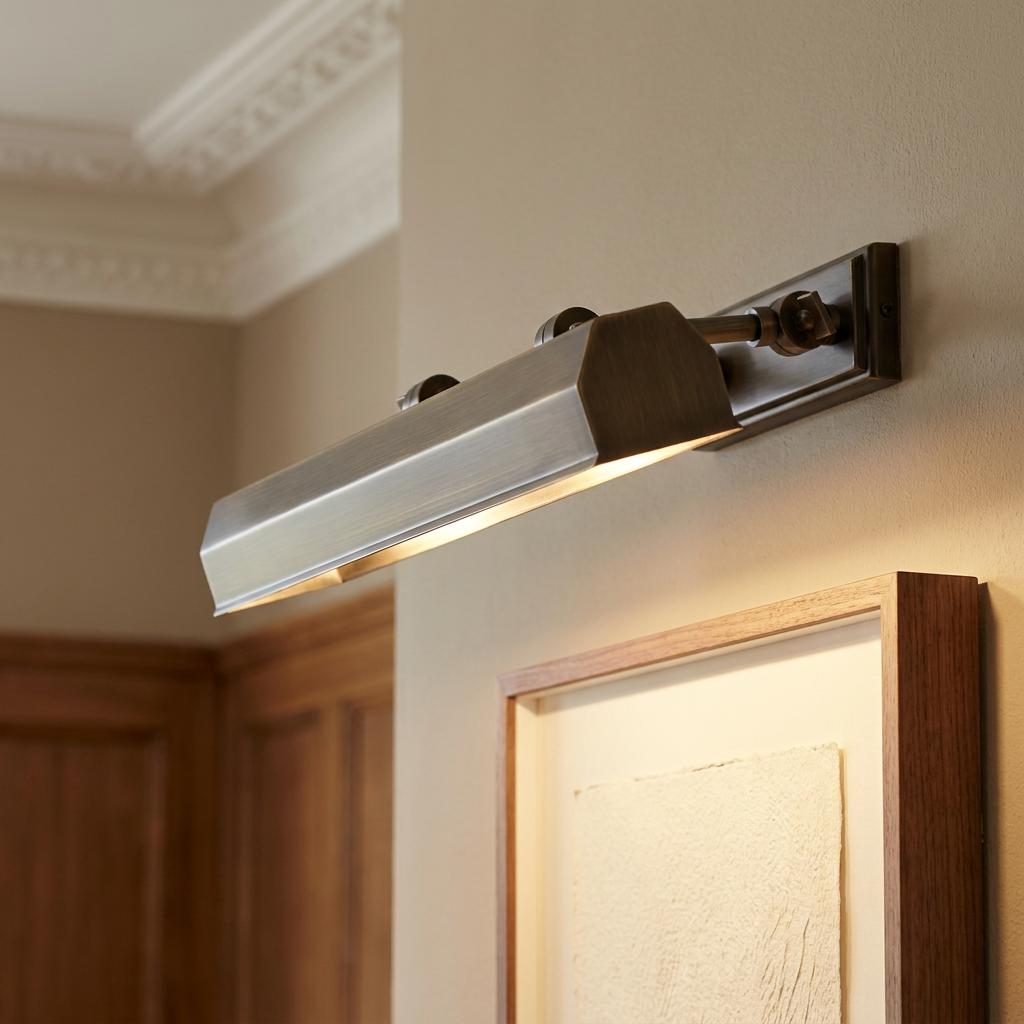 A dark bronze rectangular picture light illuminates a framed artwork from above on a neutral wall.