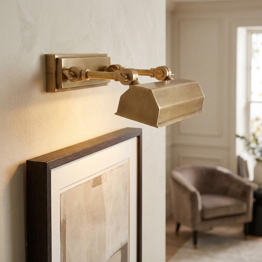 Aged brass picture light mounted on a wall, illuminating a framed artwork in a living room.
