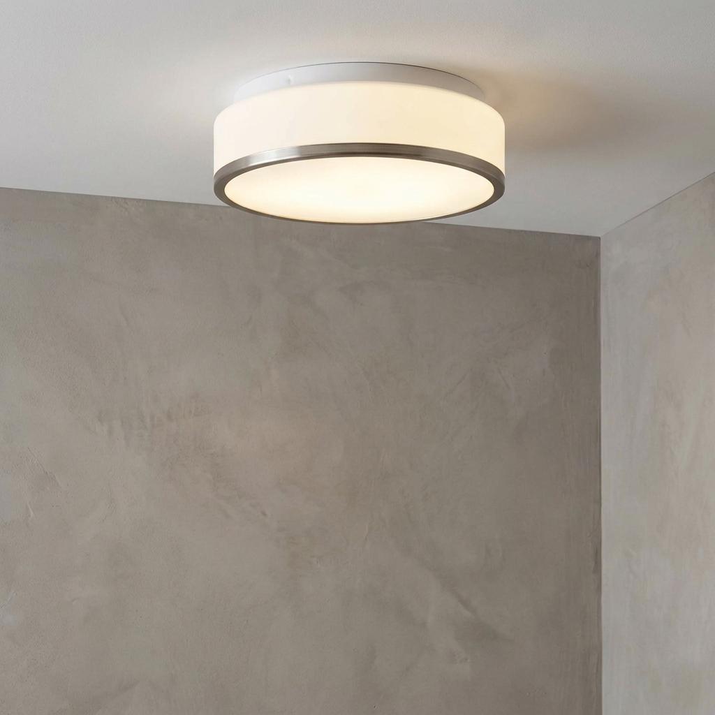 Circular opal glass flush bathroom ceiling light with a nickel trim mounted against a textured grey wall.