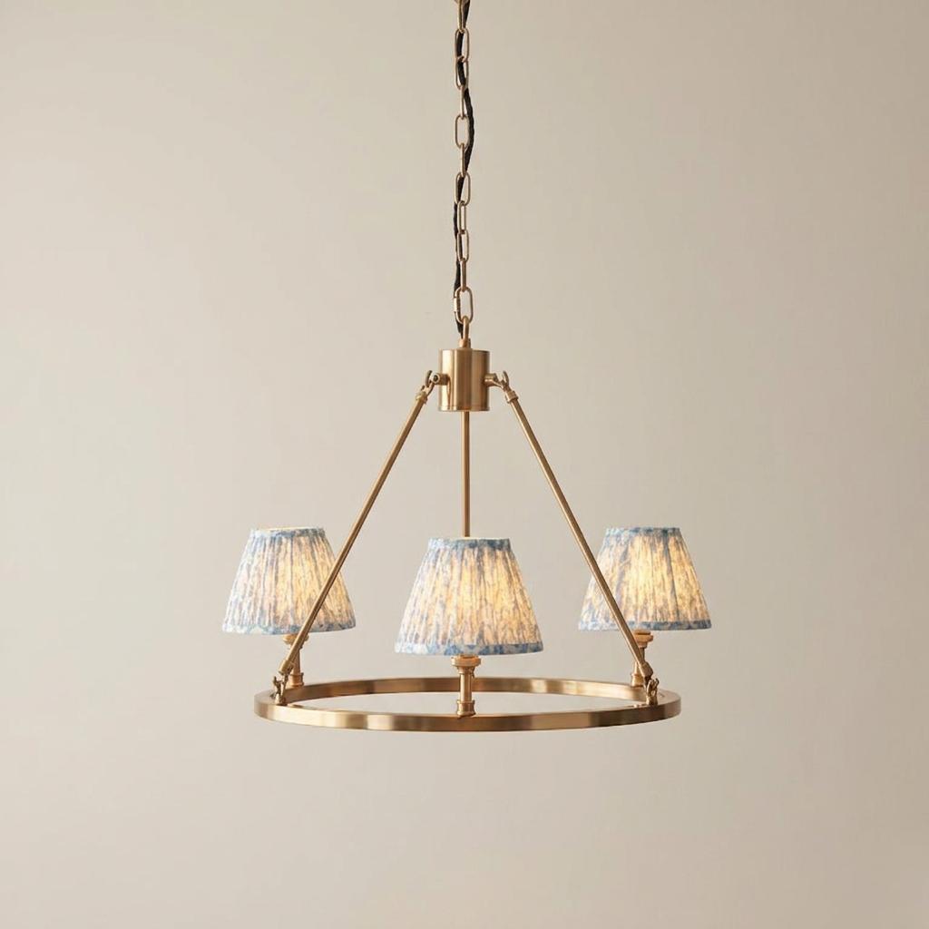 A circular brass pendant chandelier with three blue and white leaf-patterned shades suspended by a chain.