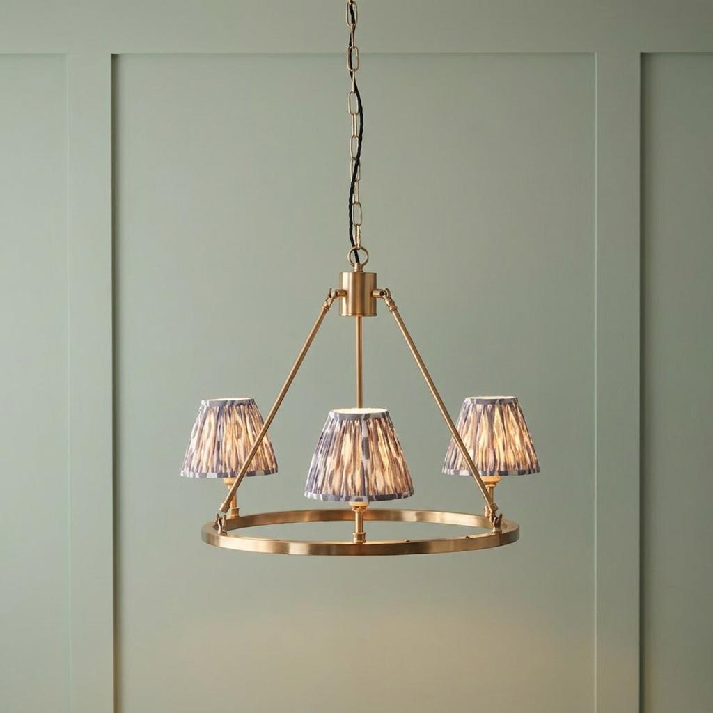 Chester brass ceiling pendant light with three pearl grey ikat shades hanging against a green paneled wall.