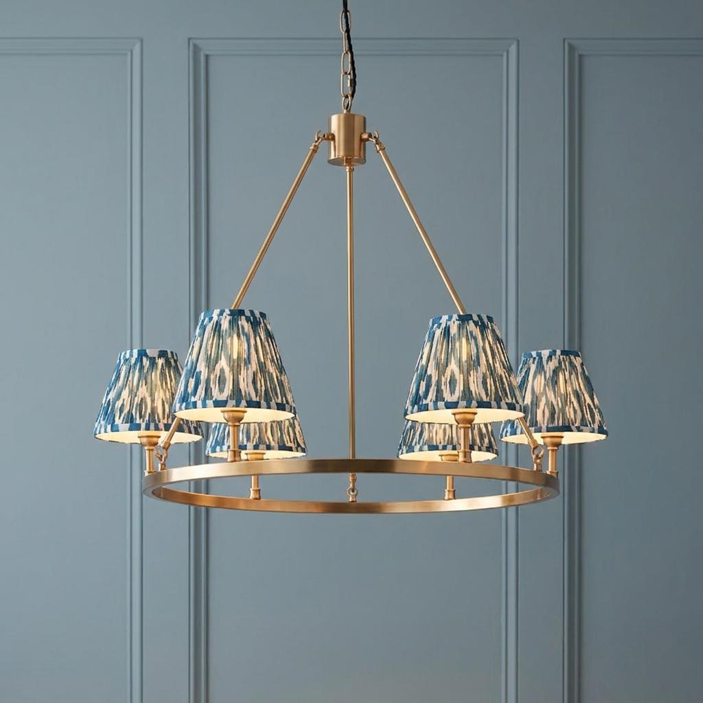 A brass hoop chandelier with blue ikat shades hanging against a pale blue paneled wall.