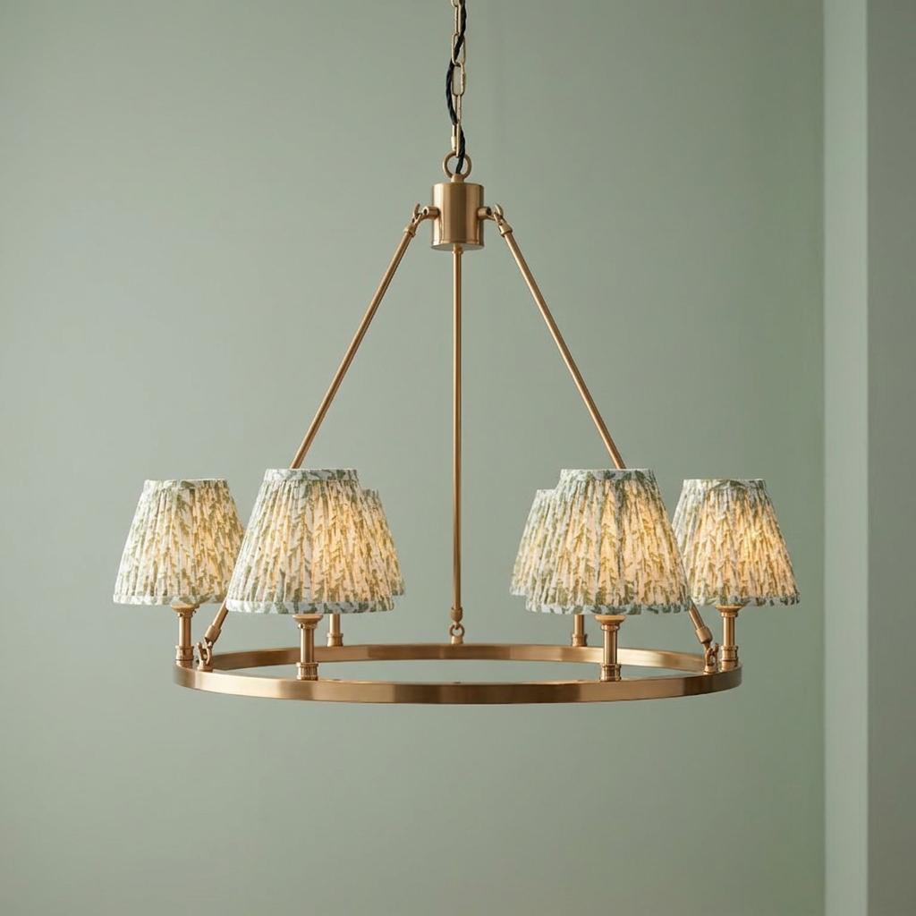 Large brass hoop chandelier with green leaf pattern pleated shades against a pale green wall.