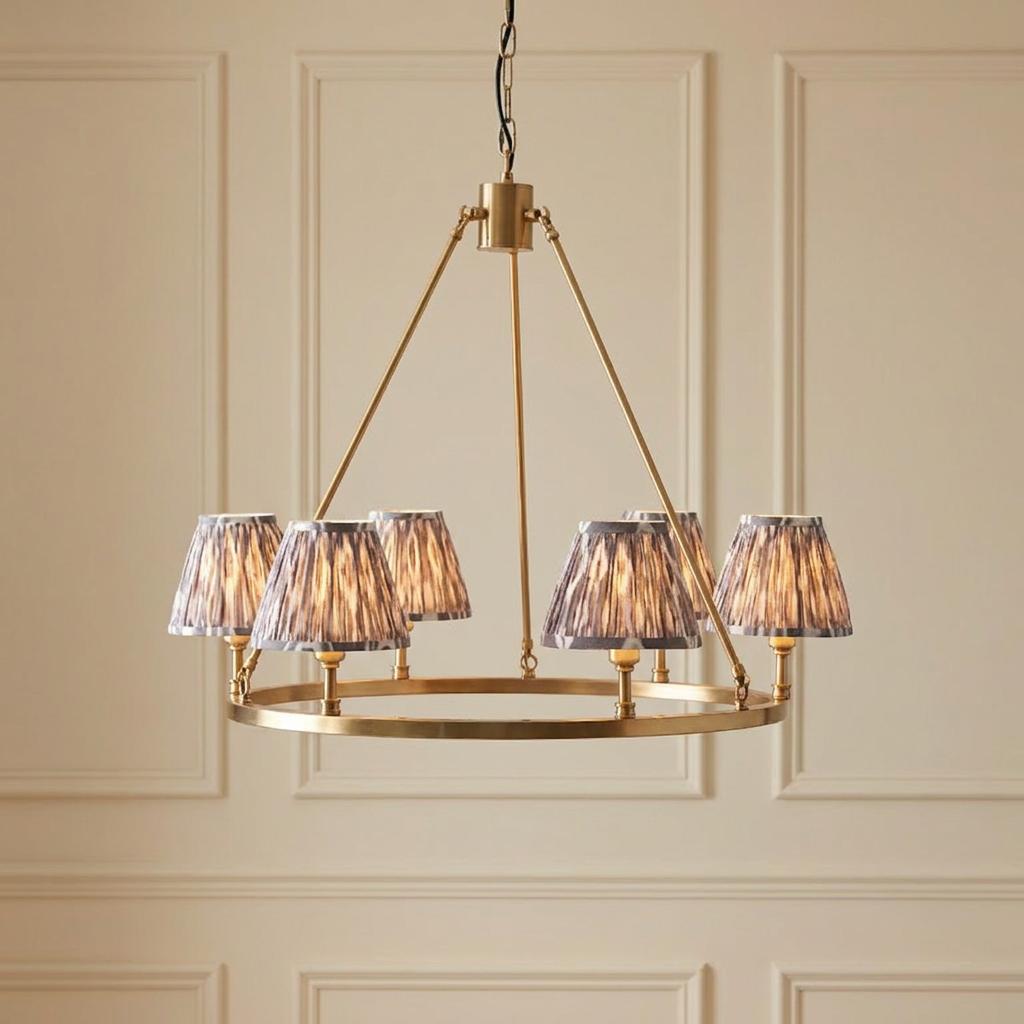 A brass hoop pendant chandelier with five grey ikat shades, hanging against a cream panelled wall.