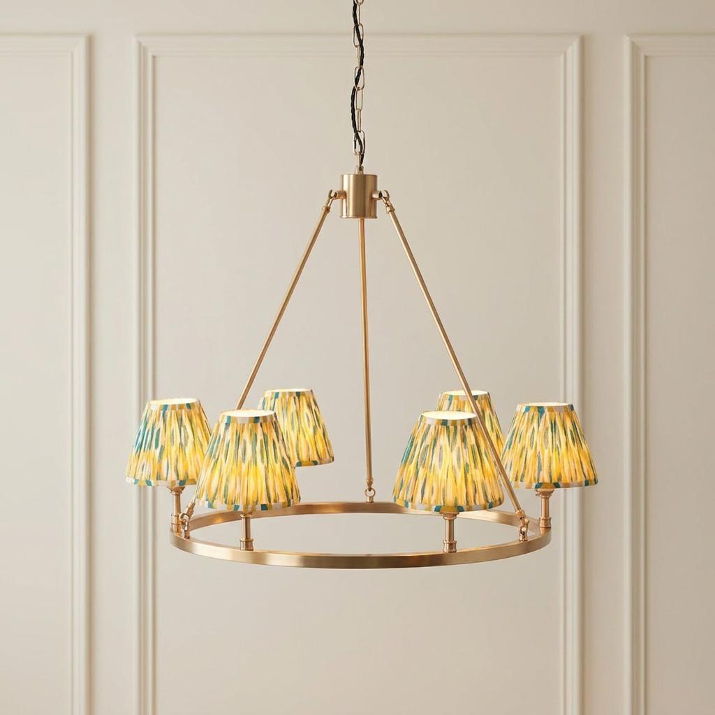 Large brass ceiling pendant with six yellow and jade ikat pattern lampshades against a neutral paneled wall.