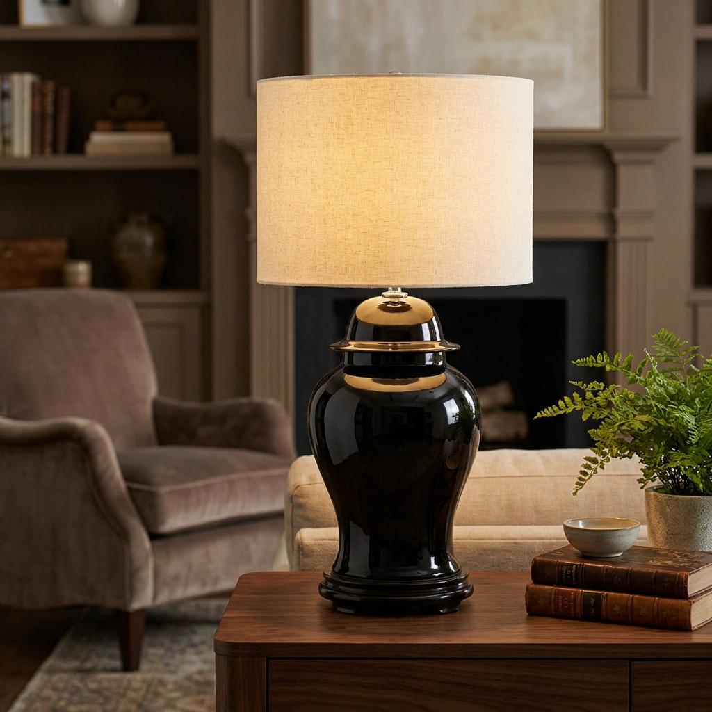 Black ceramic ginger jar table lamp with a cream drum shade on a wooden table in a classic living room setting.