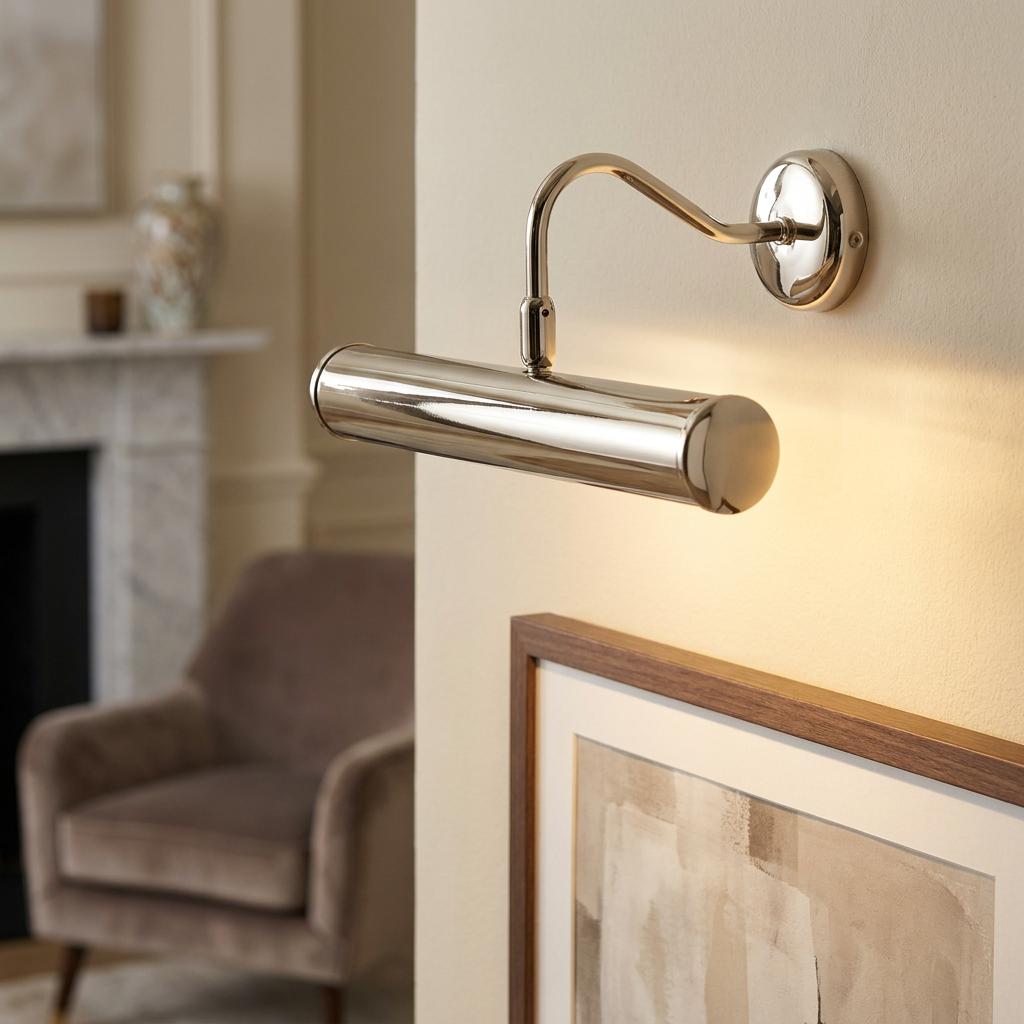 Sleek chrome picture light mounted on a wall, casting a warm glow over a framed piece of art.