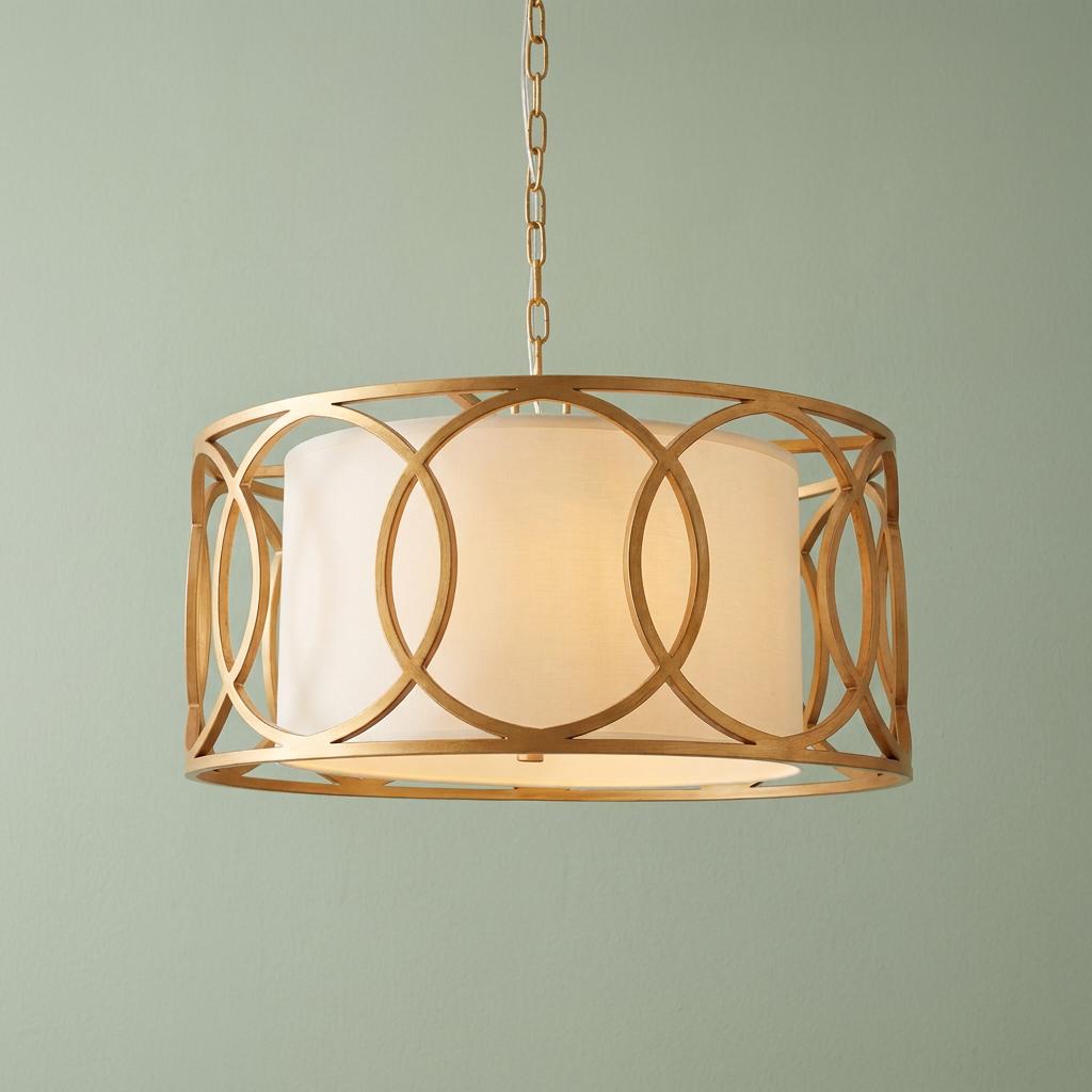 Brushed gold circular pendant light with interlocking ring frame and white fabric shade against a green wall.
