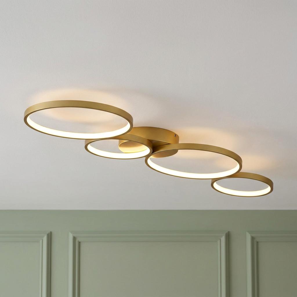 Modern gold flush-mount ceiling light with four interlocking LED rings glowing against a white ceiling.