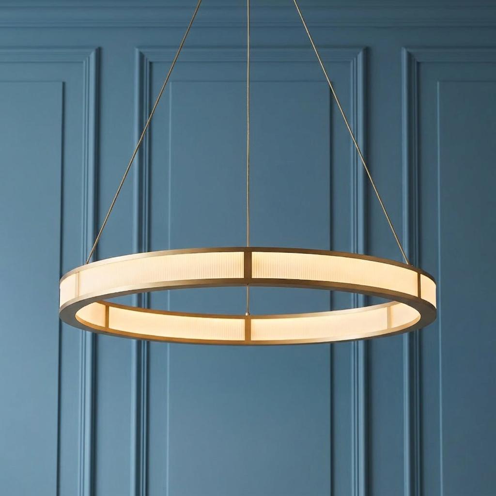 Modern gold hoop pendant light with ribbed glass panels hanging against a blue paneled wall.
