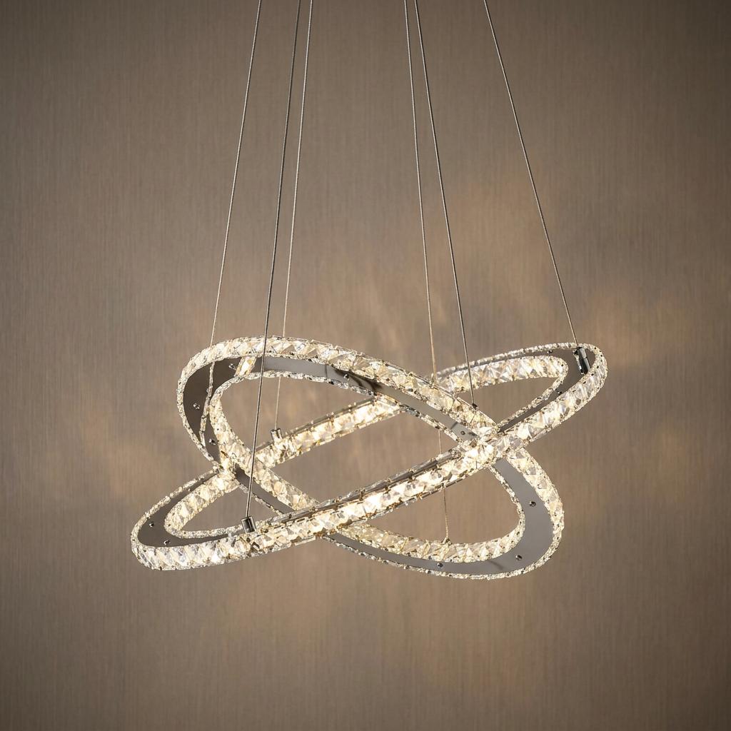 Interlocking chrome and crystal LED rings forming a modern pendant light suspended against a brown textured wall.