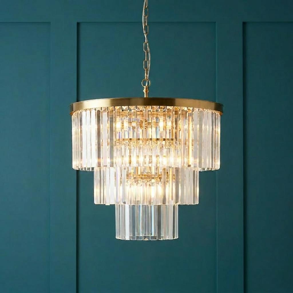 Tiered brass chandelier with vertical clear glass rods illuminated against a teal paneled wall.