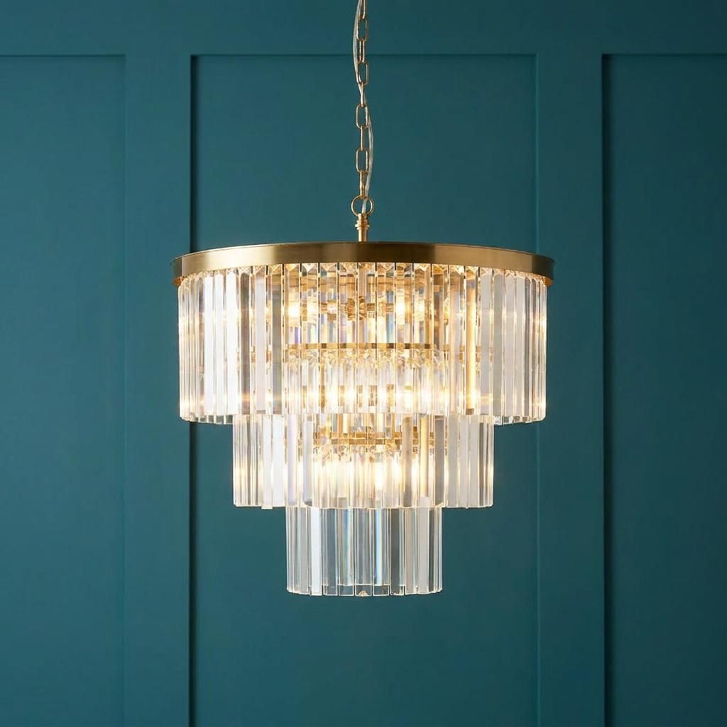 Tiered brass chandelier with clear cut glass prisms illuminated against a teal paneled wall.