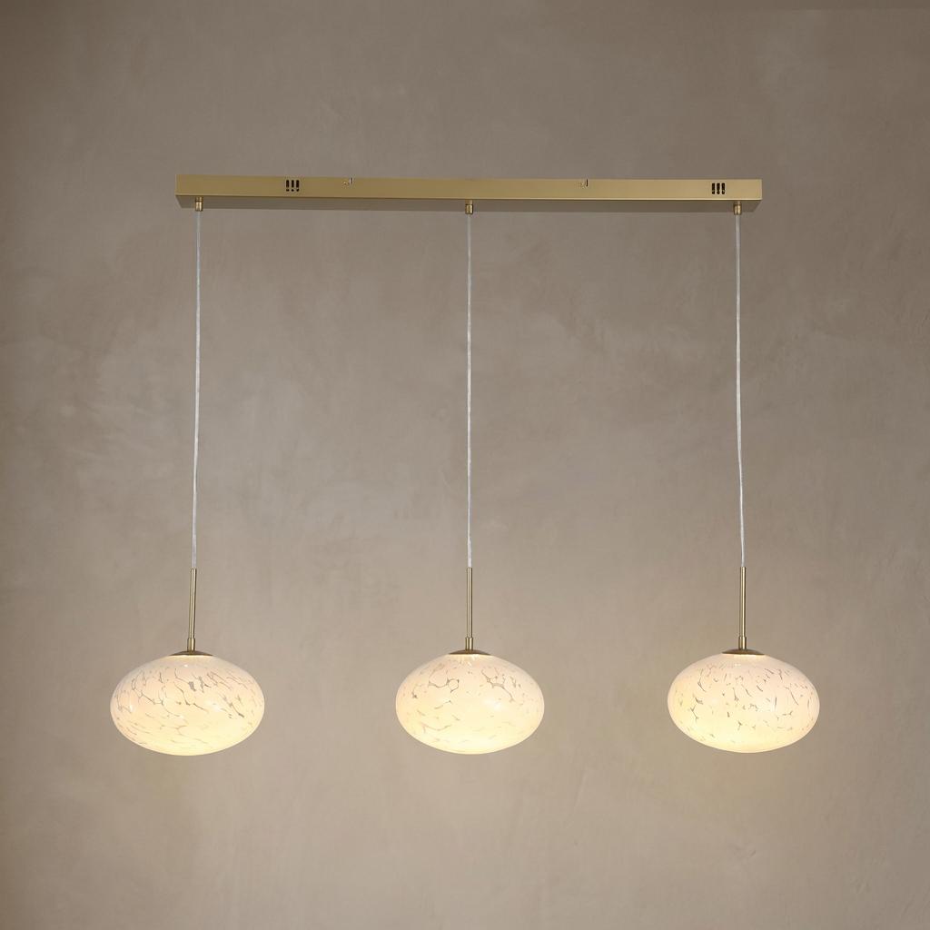 Three glowing confetti glass pendant lights suspended from a gold linear bar against a neutral textured wall.