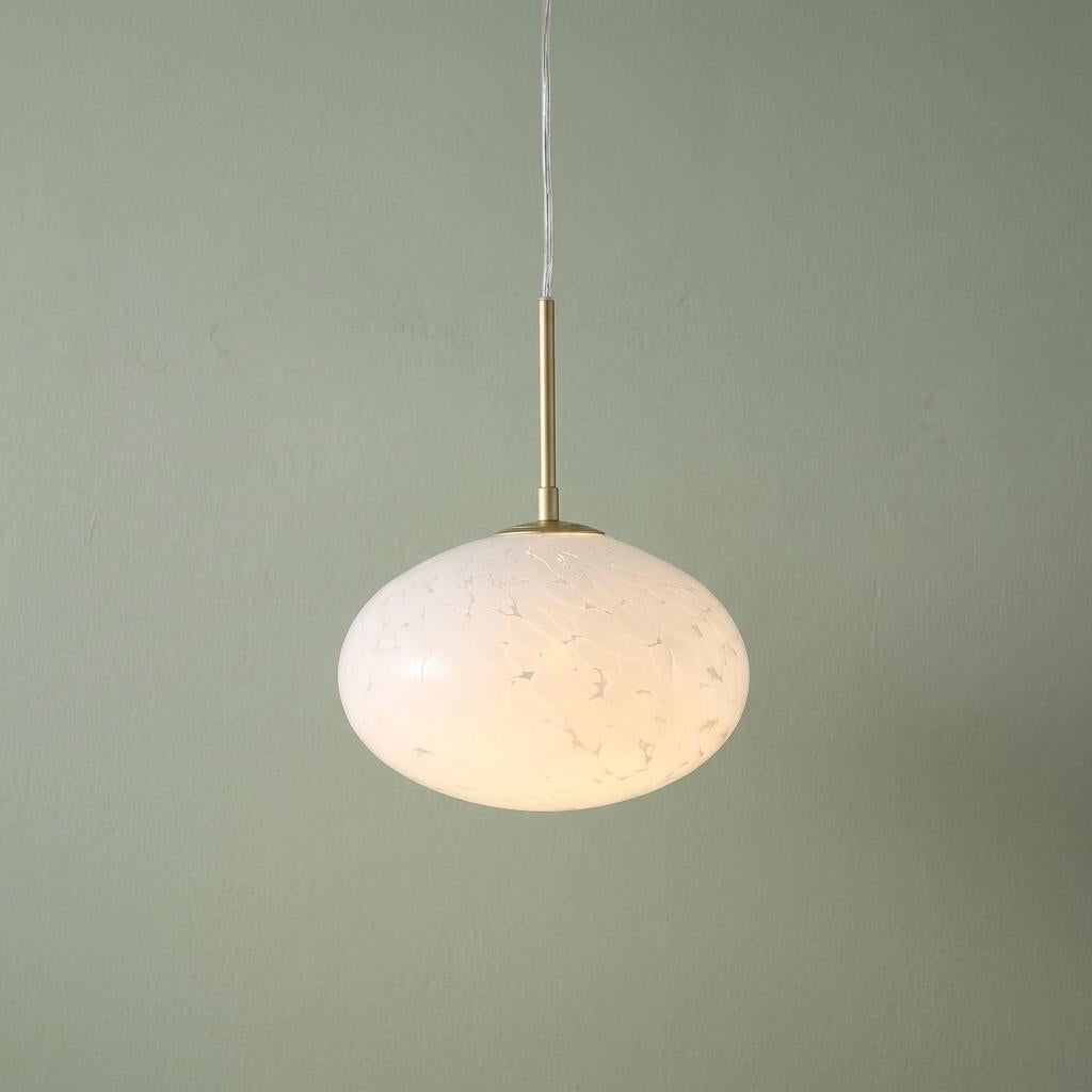 Mottled white glass oval pendant light with a gold stem against a soft green wall.