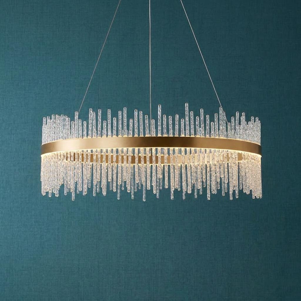 Brushed gold ring chandelier with tiered glass rods suspended against a textured teal wall.