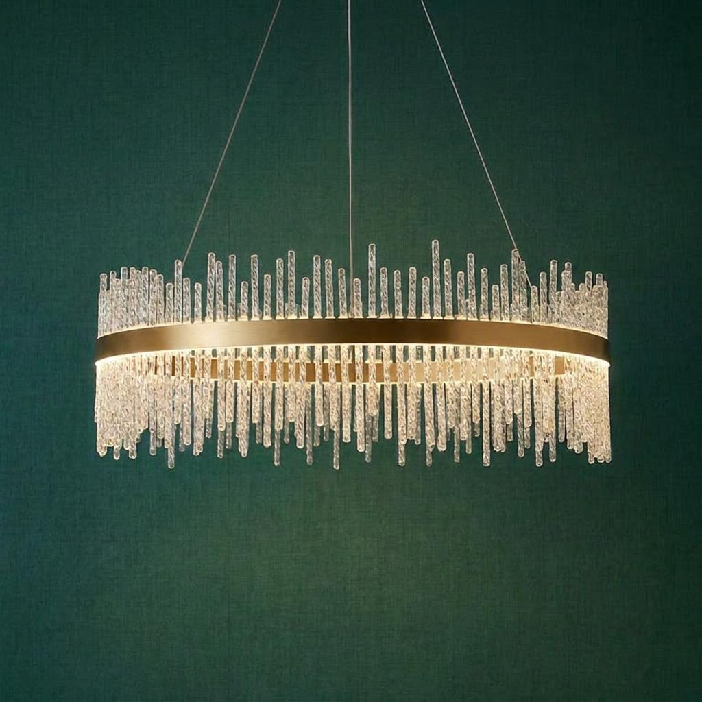 Circular brushed gold pendant light with vertical textured glass rods against a dark teal wall.