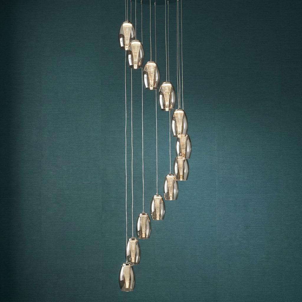 Twelve-light LED spiral multi-drop pendant with smoked glass shades against a textured teal wall.