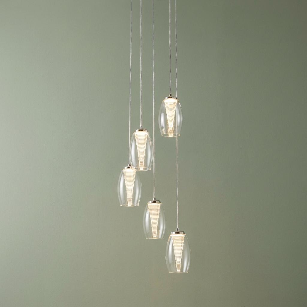 Five clear glass pendant lights with ribbed LED centers cascade against a soft green wall.