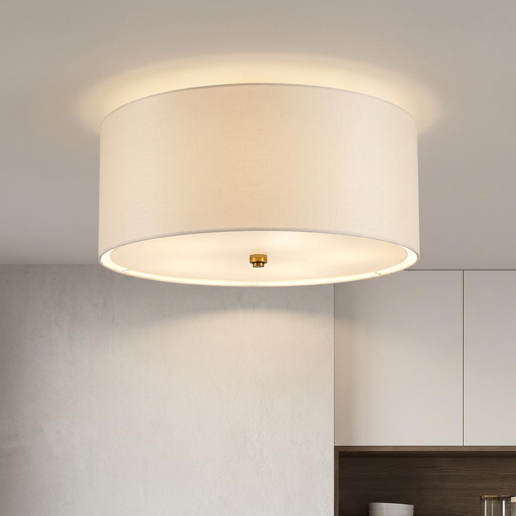 Cream fabric drum flush mount ceiling light with a brass finial glowing in a modern home interior.