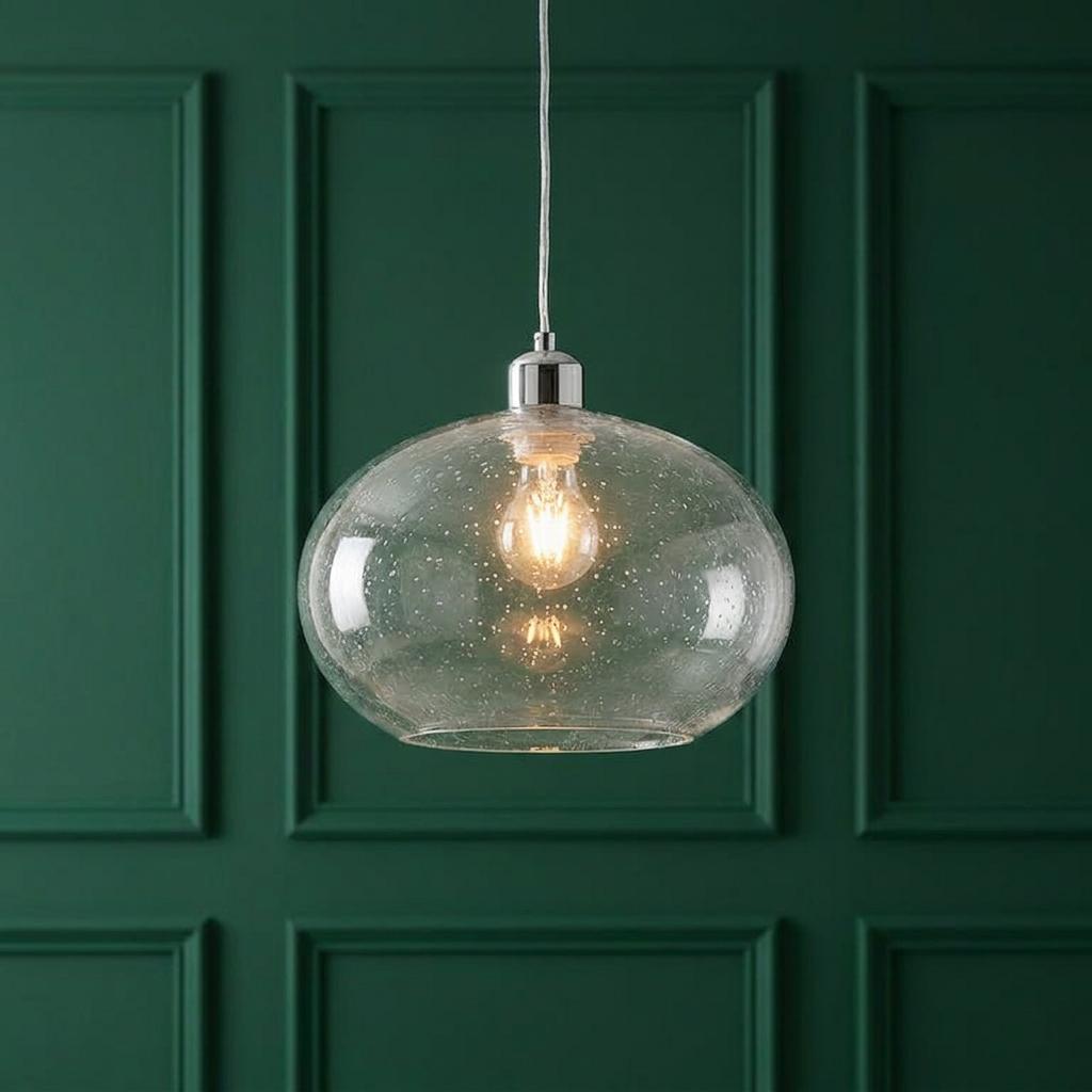 Seeded clear glass pendant light with an oval shade and chrome top, illuminated against a green wood-paneled wall.
