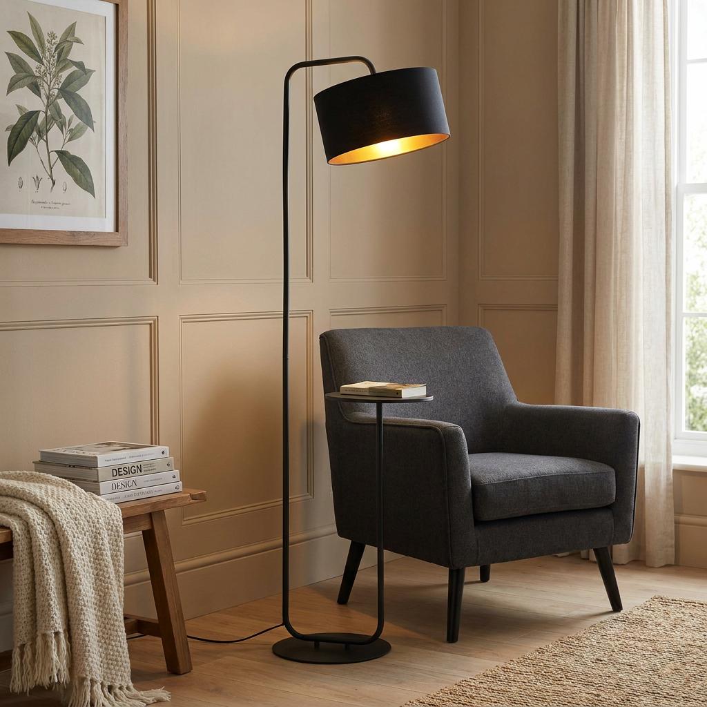 Black floor lamp with an integrated side table and gold-lined shade next to a grey armchair in a paneled room.
