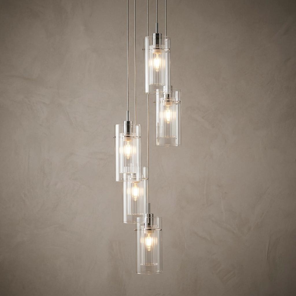 Cascading five-light pendant with chrome accents and double glass cylinders against a neutral textured wall.