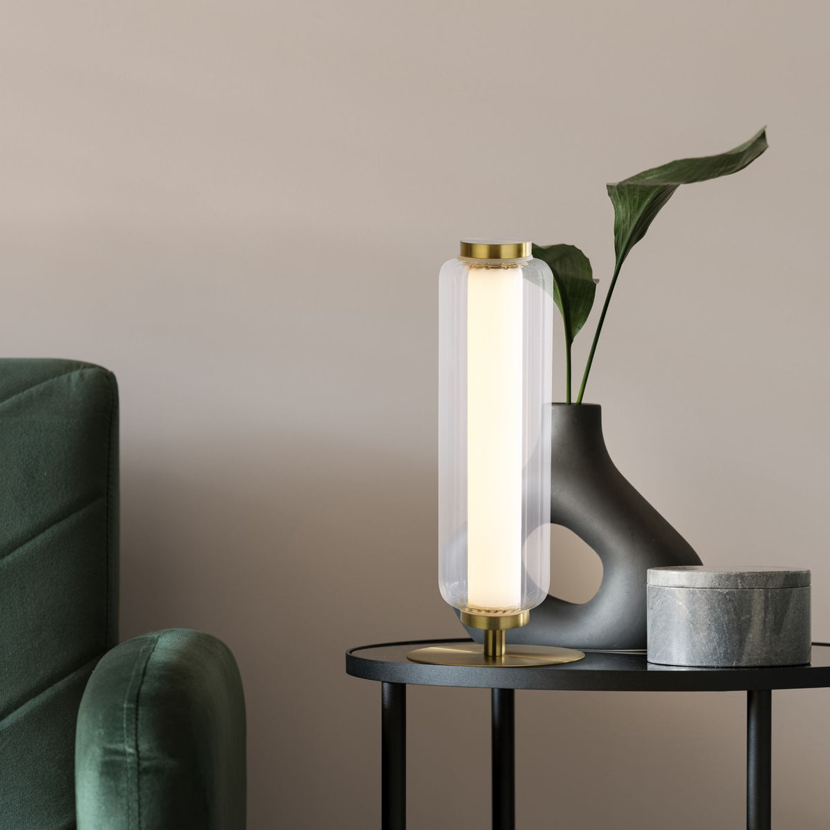 Mod brass table lamp on a black side table with green sofa grey vase and marble box