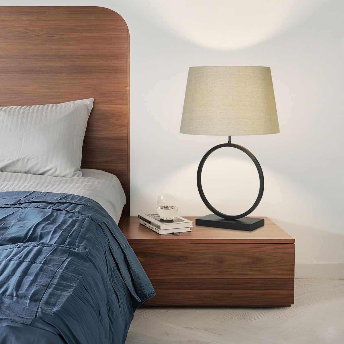 Elegant black ring lamp lit on a walnut bedside table beside a bed with blue and white bedding