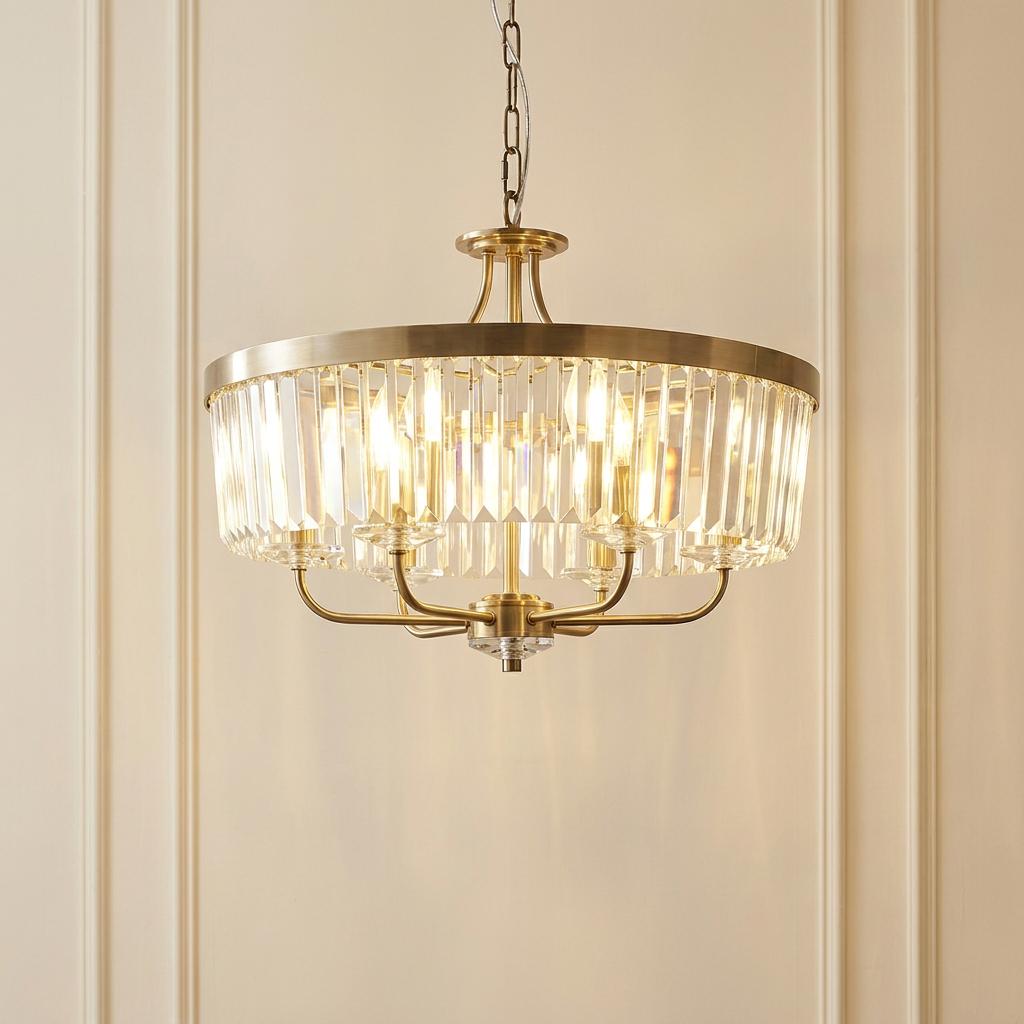 A round brass 6-light pendant with clear cut glass prisms hanging against a cream paneled wall.