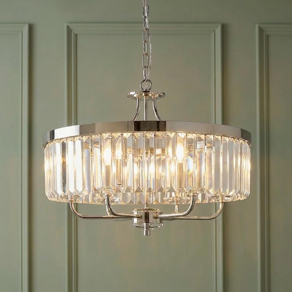 A lit 6-light chrome pendant with clear cut glass prisms hanging against a green paneled wall.