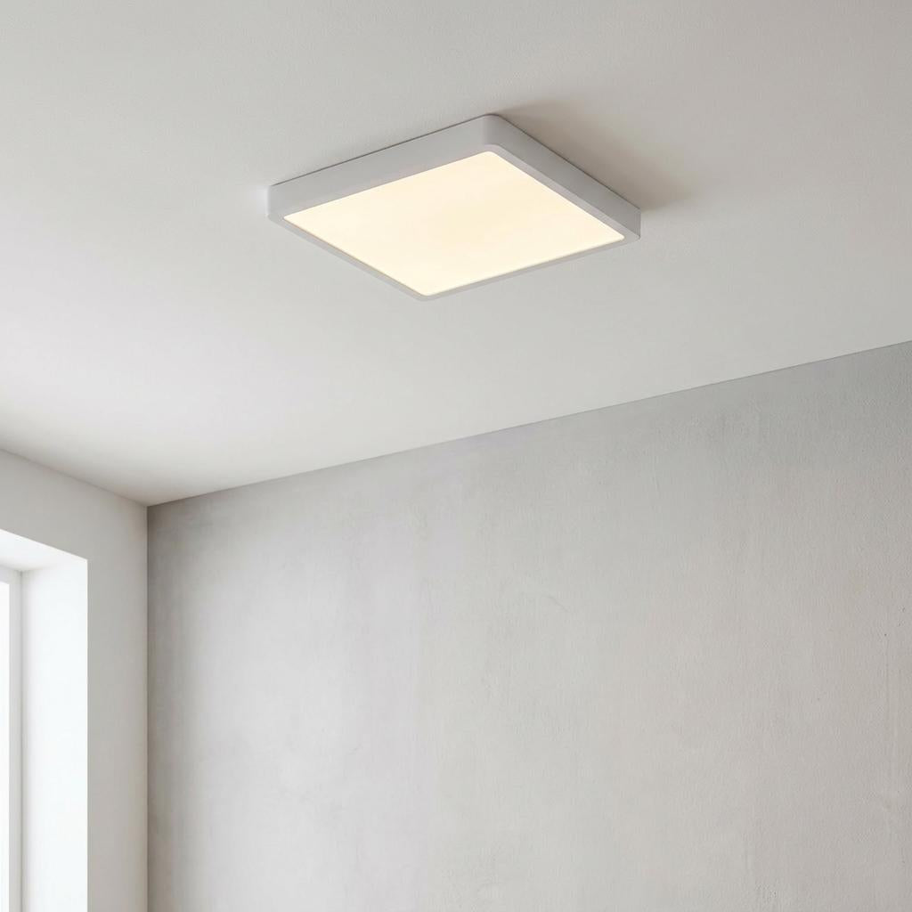 Square white LED flush mount ceiling light glowing warmly in a modern minimalist room.
