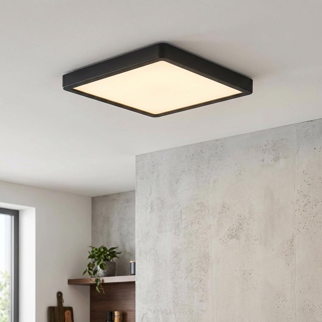 Square black flush ceiling light with a warm glow mounted on a white ceiling in a modern interior.