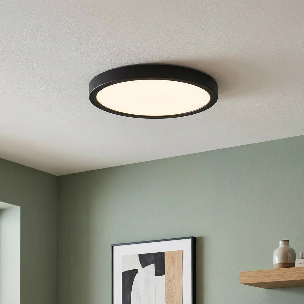 A round black flush-mount ceiling light casting a warm glow in a modern room with sage green walls.