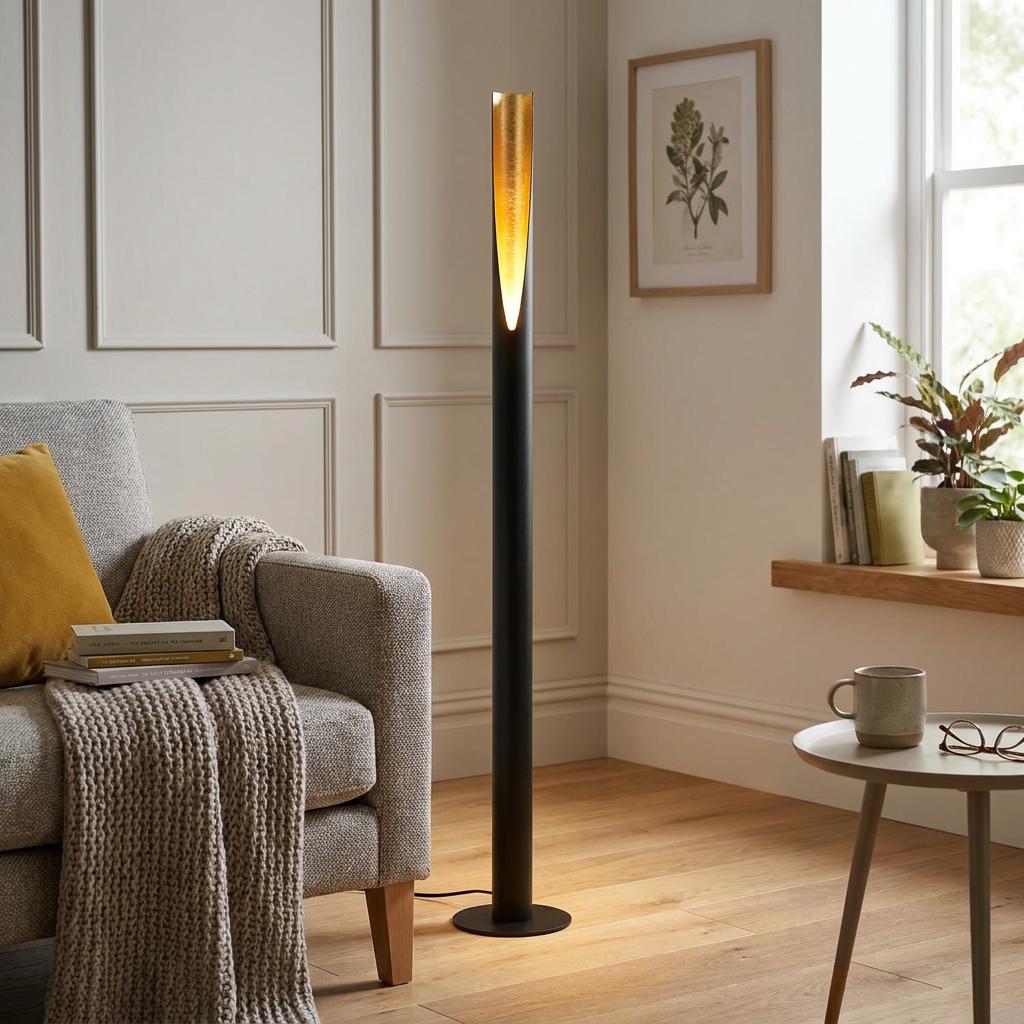 Sleek black floor lamp with a gold leaf interior top standing in a cozy living room by a grey armchair.