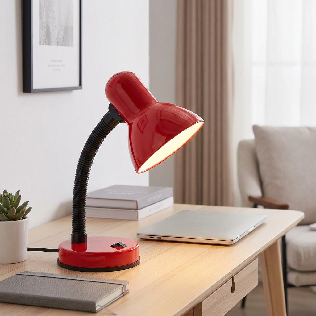 Red adjustable desk lamp illuminated on a wooden table with a laptop and books in a modern home office.