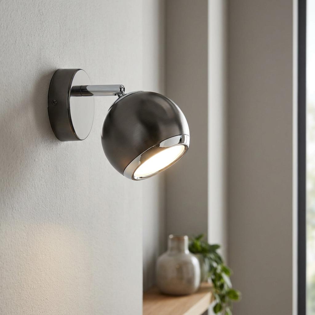 Eglo Bimeda black nickel and chrome wall spotlight mounted on a textured wall, emitting a warm glow.