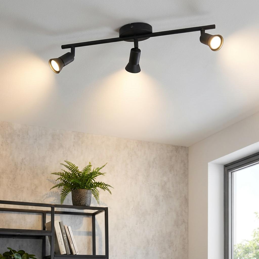 Black three-light bar spotlight mounted on a white ceiling, casting warm light in a modern room.