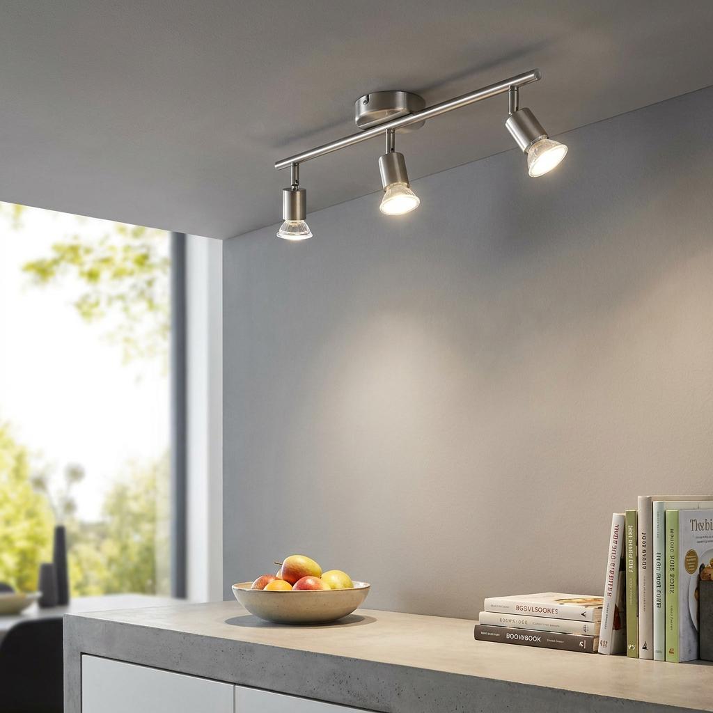 Satin nickel three-light bar spotlight mounted on a ceiling above a kitchen counter with a fruit bowl.