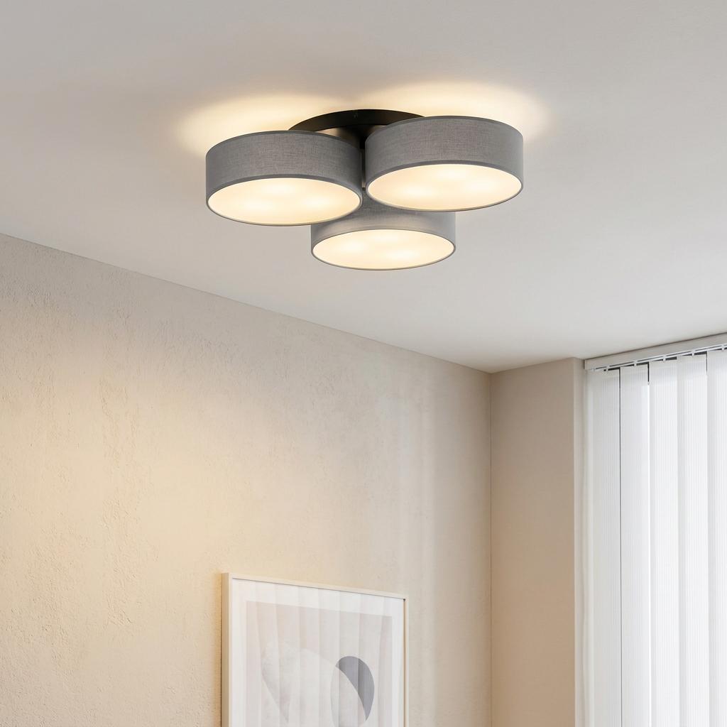 A three-light flush ceiling fixture with grey drum fabric shades glowing in a modern neutral room.