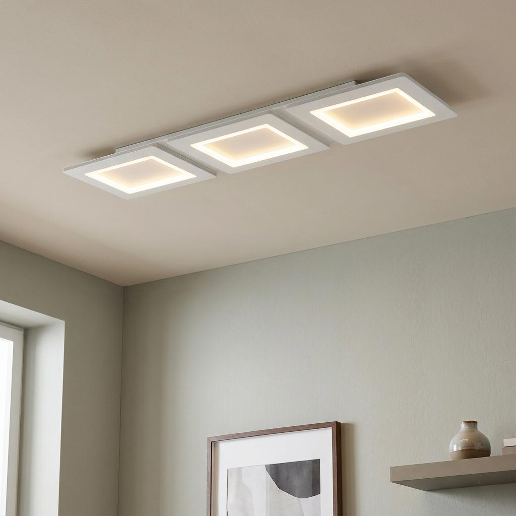 Three glowing square LED panels flush-mounted on a ceiling in a contemporary interior.