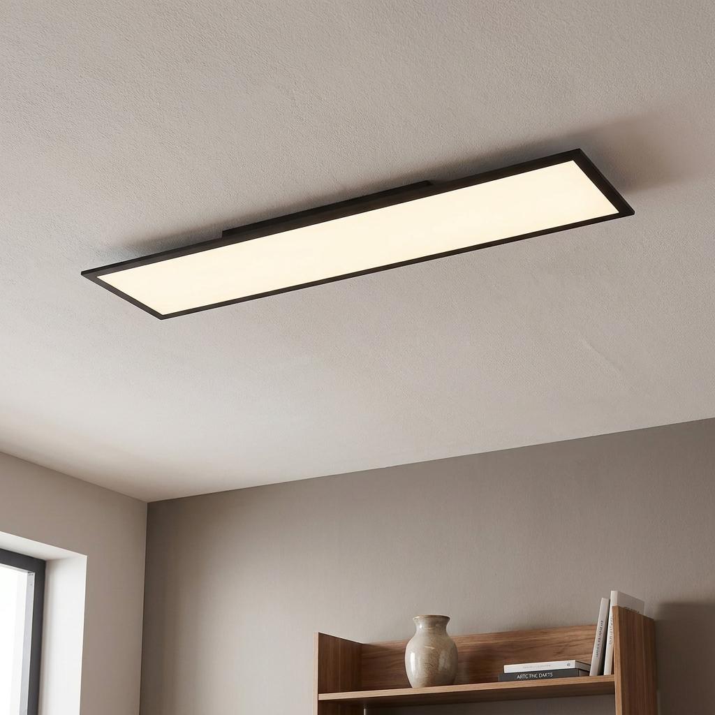 A long rectangular LED ceiling panel with a black frame glows on a beige ceiling above a wooden shelf.