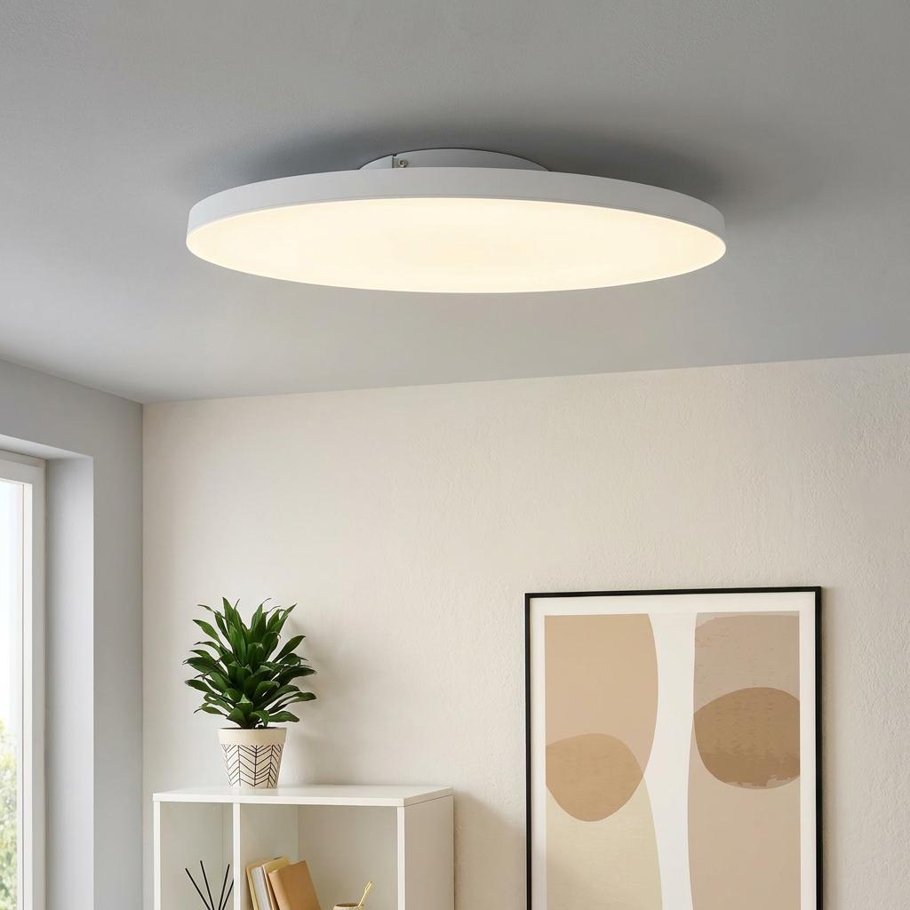 Large white round LED flush ceiling light glowing in a modern room above a plant and framed art.