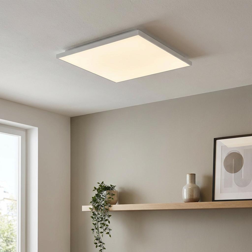 Square white LED flush mount ceiling light glowing in a minimalist room with a wooden shelf.