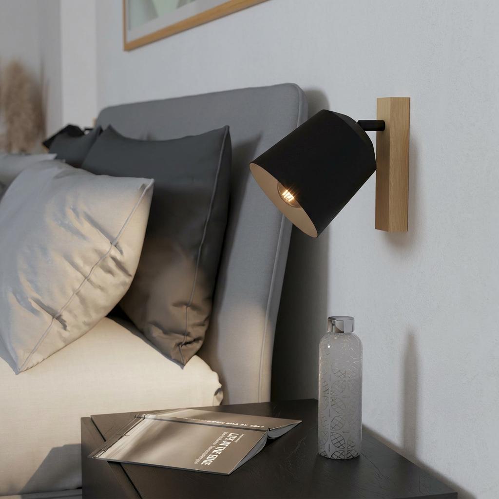 Black conical wall spotlight with a light wood base mounted beside a bed in a modern bedroom.