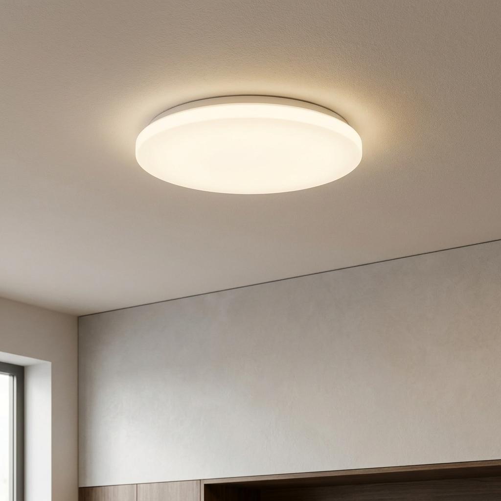 Round white LED flush ceiling light illuminated on a minimalist ceiling in a modern interior.