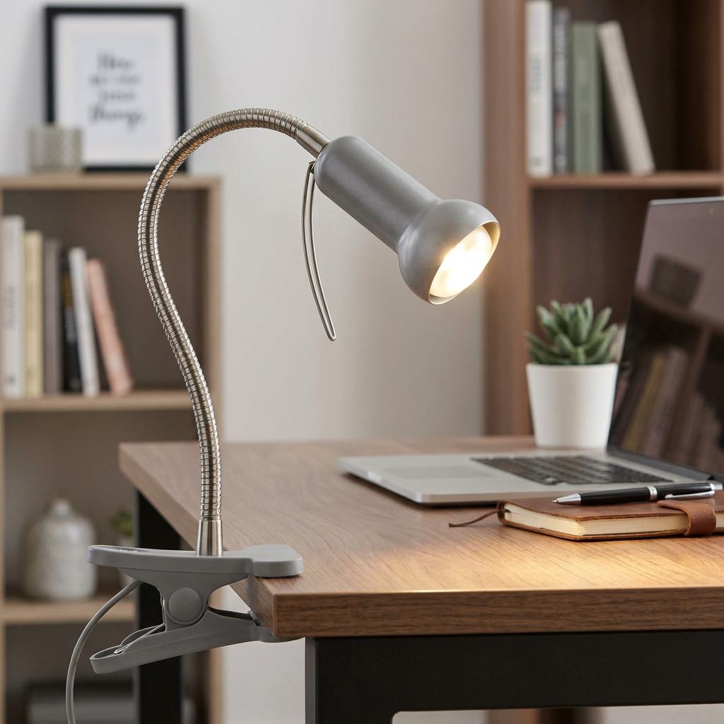 Silver task lamp with flexible neck clamped to a wooden desk, illuminating a notebook and workspace.